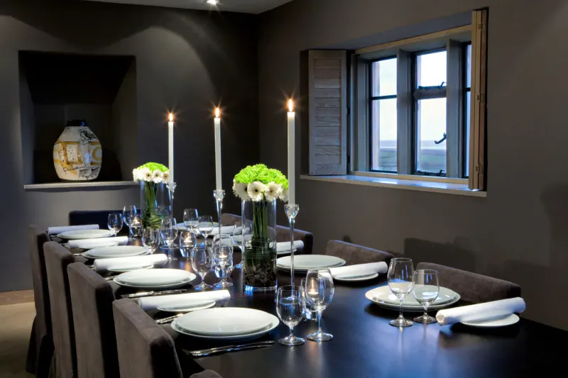 Elegant dining room at Roch Castle with long dark table set for dinner, white flowers, candles, and large window.