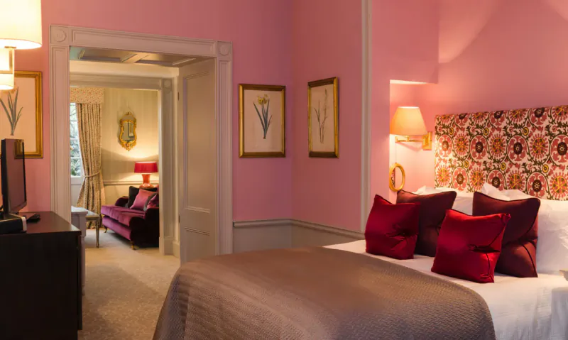 Elegant pink bedroom at Royal Crescent Hotel with floral headboard, red pillows, TV, and lounge area
