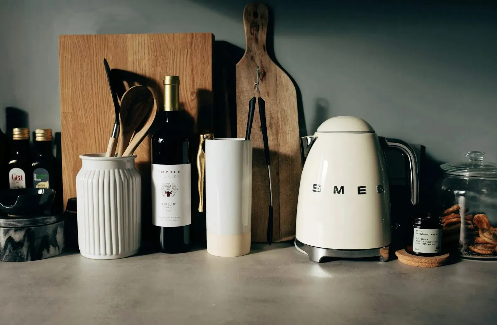 Kitchen counter with Smeg kettle, red and white wine bottles, oil jars, wooden utensils, and cutting boards.
