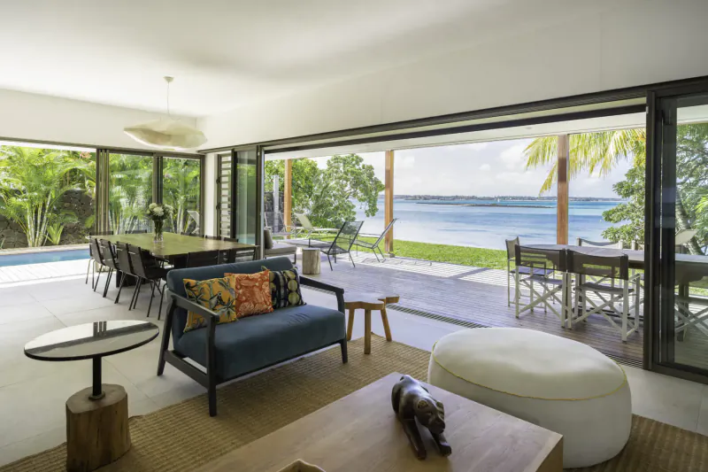 Spacious modern living room in Villa Sapphire, Mauritius, with blue sofa, wood table, open doors to pool deck and Belle Mare beach.