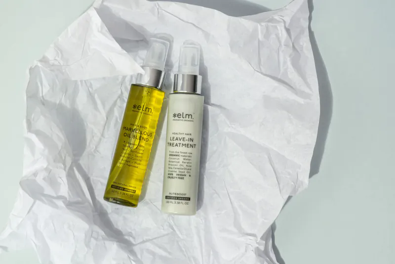 Elm Organics Norway oil serum and cleanser bottles on white fabric, sustainable luxury amenities.