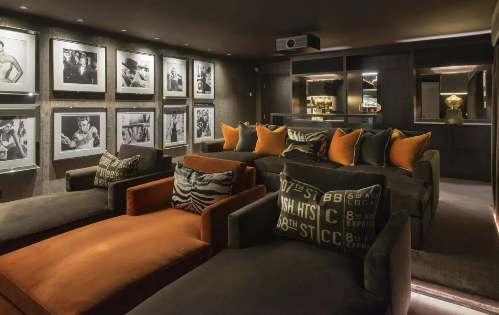Luxurious home theater with orange and gray lounge seats, black-and-white framed photos on walls, and projector.