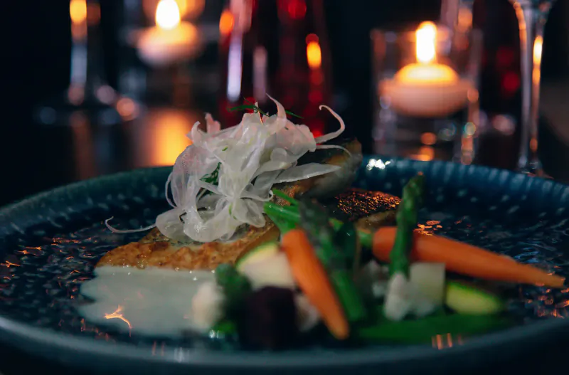 Pan-fried white fish with asparagus, carrots, daikon on blue plate, lit by candles at Lio Cabaret restaurant.