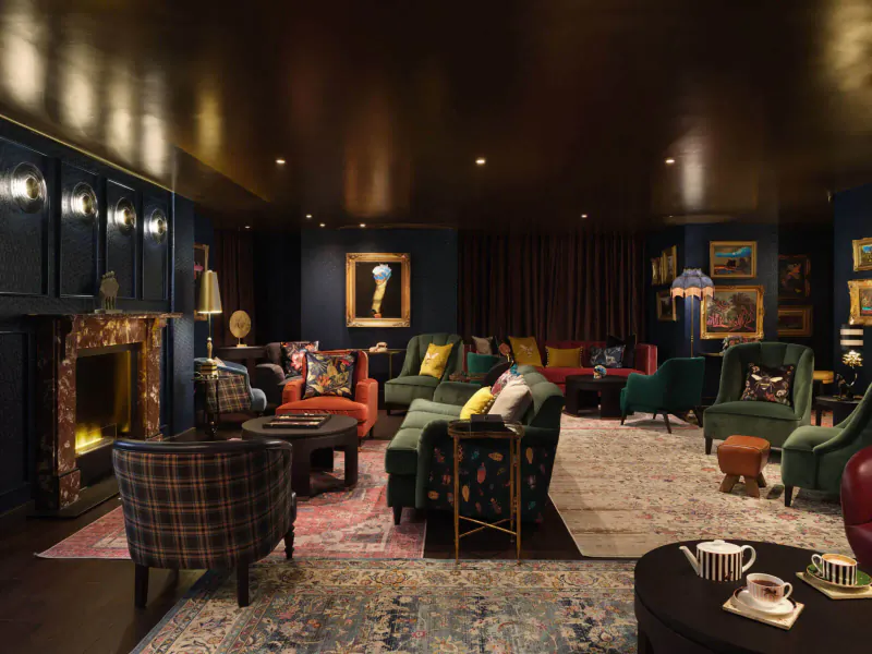 Luxurious gallery lounge with dark walls, colorful velvet sofas, patterned rugs, fireplace, and art.