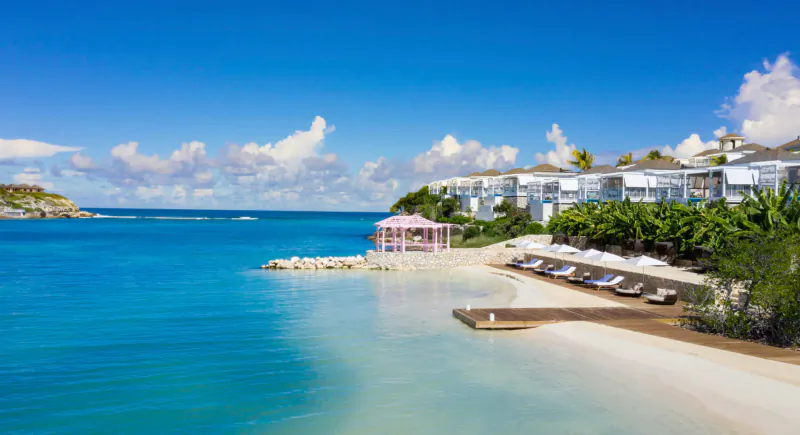 Aerial view of Hammock Cove luxury resort in Antigua: white villas, pink beach gazebo, lounge chairs, turquoise sea, and sandy shore.