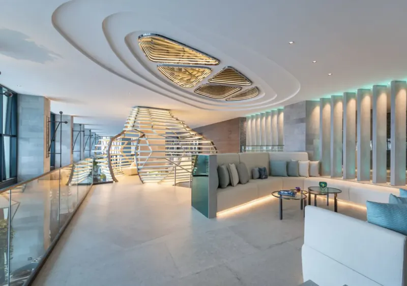 Modern W Algarve hotel interior with sculptural golden ceiling, spiral glass staircase, teal lounge seating, and columns.