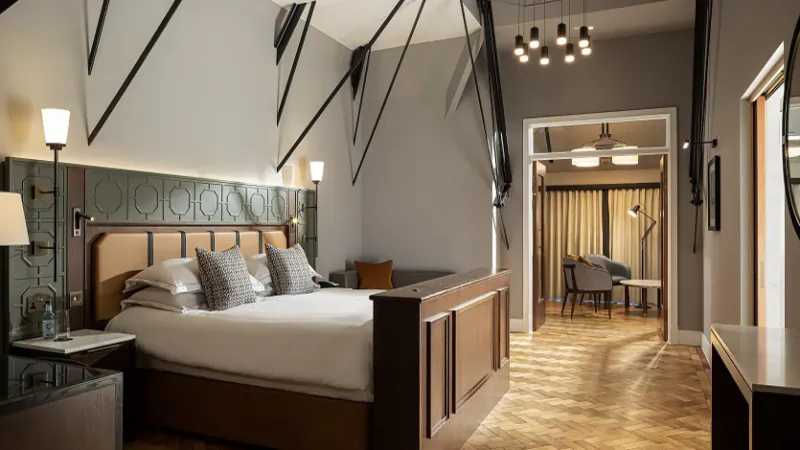 Luxury hotel suite at The Parkgate Hotel with king bed, exposed beams, pendant lights, and lounge area.