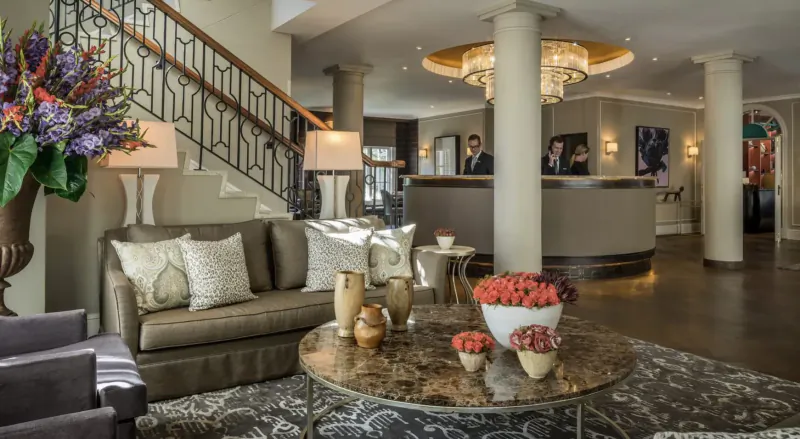 Elegant Four Seasons Westcliff hotel lobby in Johannesburg with curved reception desk, grand staircase, chandelier, plush seating, and floral arrangements.