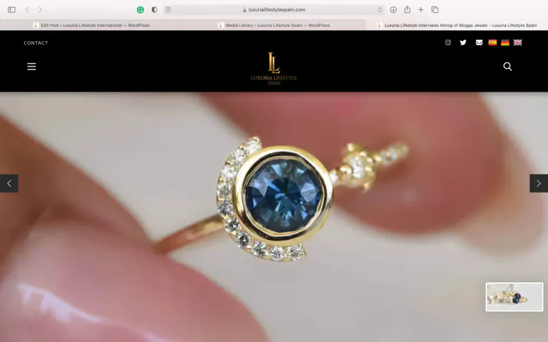 Close-up of Mogga Jewels gold ring with blue gemstone and diamonds held in fingers, on website homepage