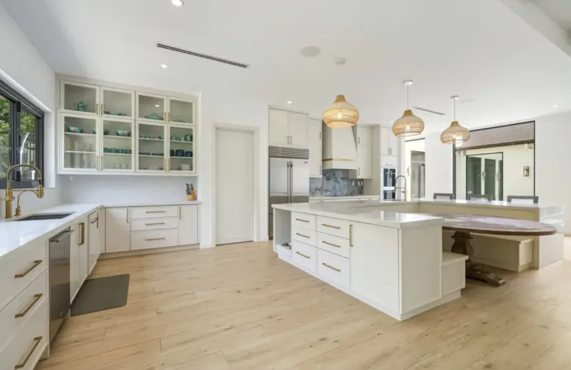 Modern white kitchen with large island, woven pendant lights, glass cabinets, and wood floors in Lyford Cay home