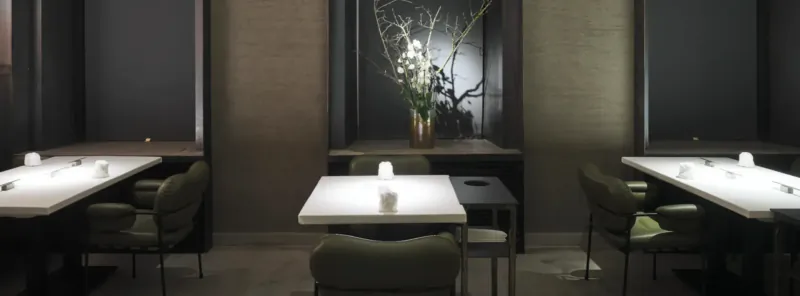 Elegant modern dining room with white tables, green chairs, candles, and tall white flower arrangement in Vienna gallery