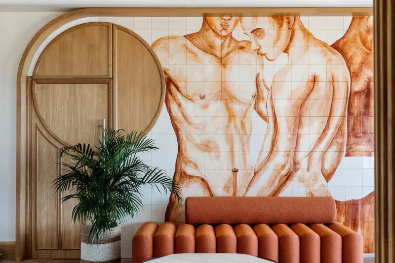 Hotel Riomar lobby with mural of embracing nude male figures, curved wooden door, potted palm, orange curved bench