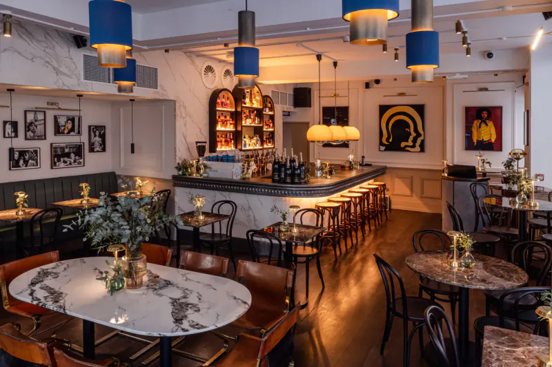 Ziggy Green: Vibrant London bar and restaurant interior with marble bar, stools, pendant lights, art, and plants.