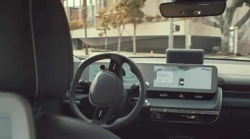 Driver's view in Hyundai IONIQ 5 robotaxi, steering wheel and navigation display active on urban street.