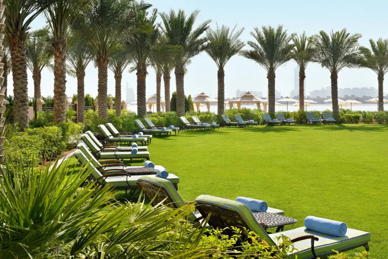 Luxury resort poolside lounge chairs with blue towels on lush green lawn, palm trees, and sea view
