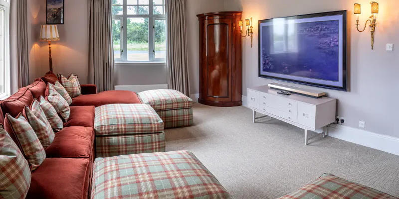 Luxury living room in Fairmont St Andrews Manor Home with red plaid L-shaped sofa, large wall-mounted TV, and window views.