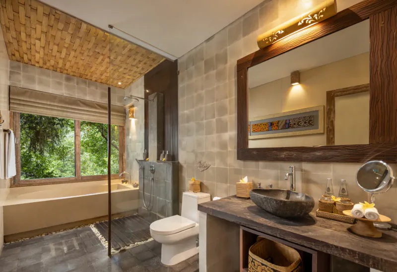 Luxurious Balinese bathroom at Kayon Resort with stone sink, bathtub, large mirror, and jungle view window.