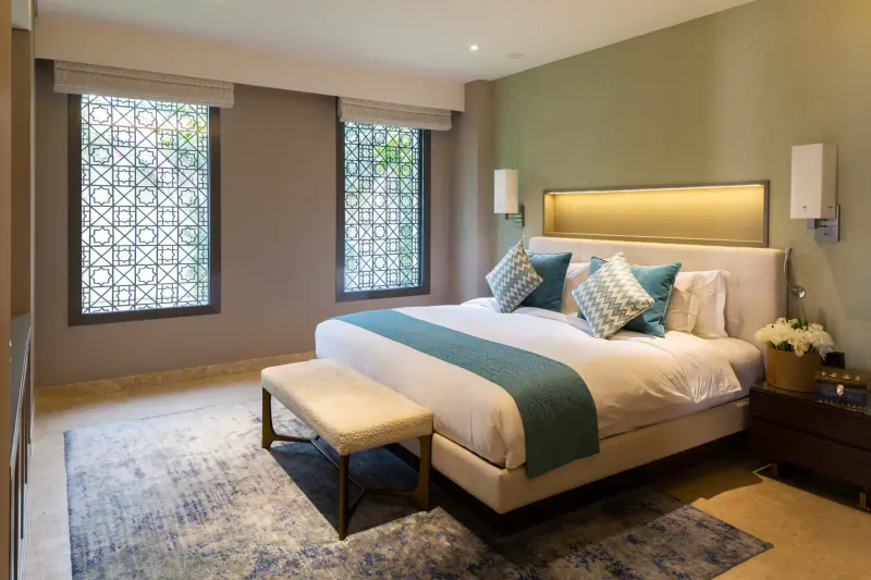 Luxurious bedroom in Melia Desert Palm Dubai with teal-accented king bed, lattice windows, and beige tones.