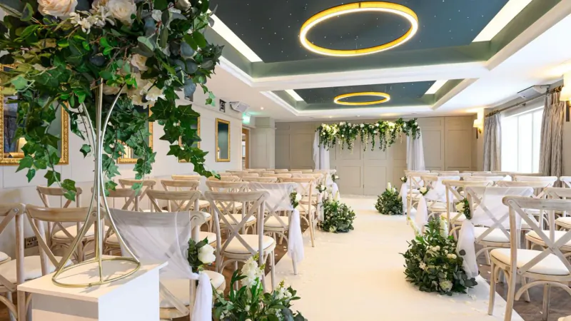Elegant wedding venue with rows of white chiavari chairs, floral arches, and greenery in a modern room at Manor House Hotel.