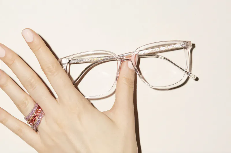 Hand holding clear frame glasses, wearing pink gemstone ring, white background, Pair for Pair scheme
