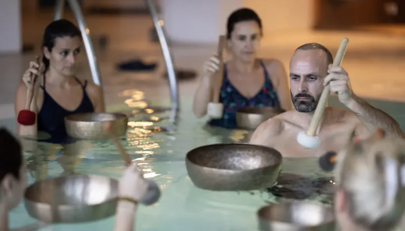 Group in pool playing Tibetan singing bowls with mallets during sound bath session.