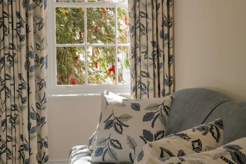 Window with floral-patterned curtains and pillows in elegant hotel room, garden view outside.