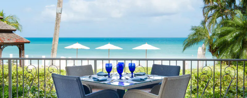 Table set with blue glasses and plates on terrace overlooking Caribbean beach, palms, and umbrellas at Blue Waters Resort.