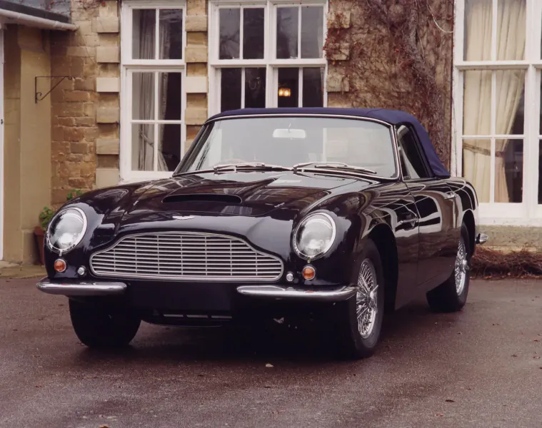 Black Aston Martin DB4 convertible parked in front of stone manor house at concours d'elegance