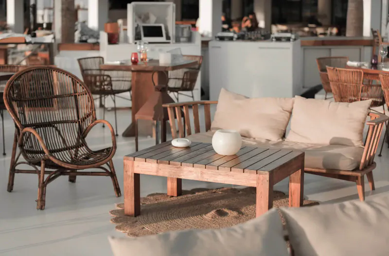 Cozy wicker outdoor lounge seating with wooden table, white vase, and cushions at Destino Pacha Ibiza beach bar.