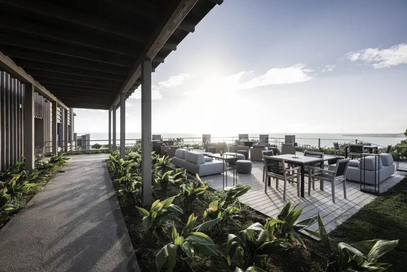 Outdoor terrace at ADLER Spa Resort Sicily with lounge seating, tables, plants, and sea view at sunset