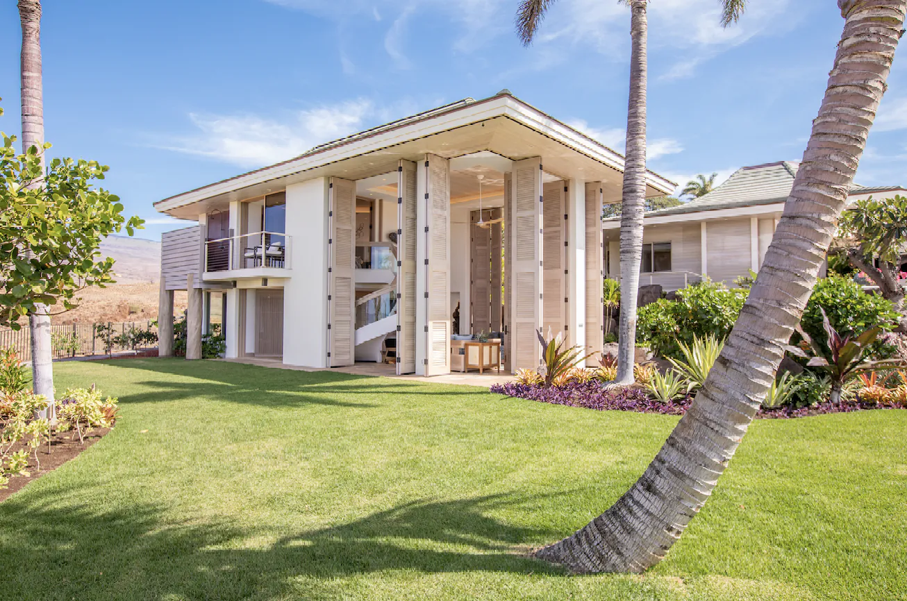 Modern luxury white house with palm trees, lush lawn, and tropical landscaping under blue skies