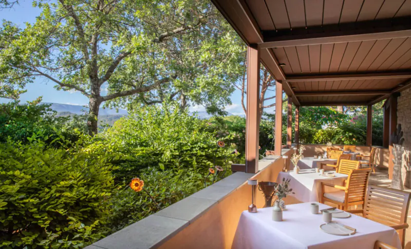 Outdoor terrace at Terre Blanche resort in Provence with wooden tables set for dining, overlooking lush green hills and mountains.