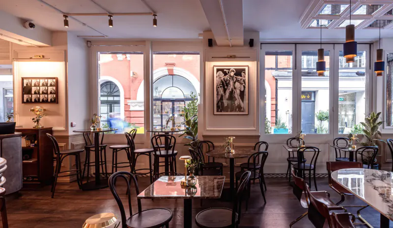 Ziggy Green cafe interior in London: elegant wooden tables, black chairs, plants, black-and-white art on walls, large arched windows.