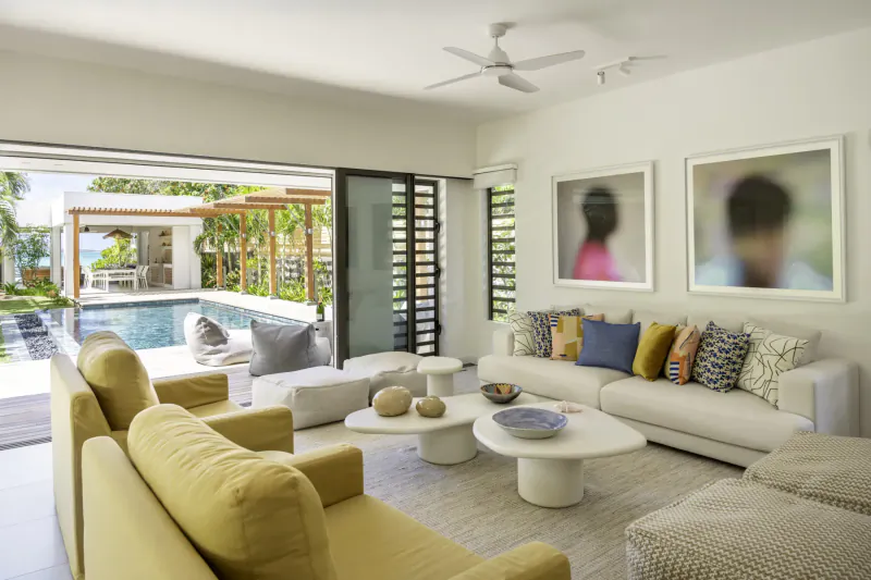 Spacious modern living room in Villa Diamond, Mauritius, with yellow sofas, white coffee tables, pool view, and large portraits.
