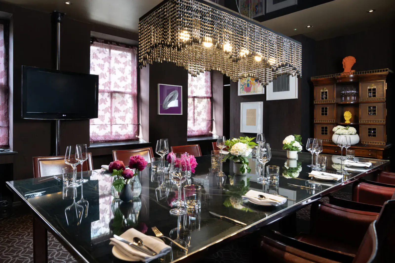 Elegant dining room at Pied à Terre with long black table set for meal, pink peonies, wine glasses, chandelier, and art.