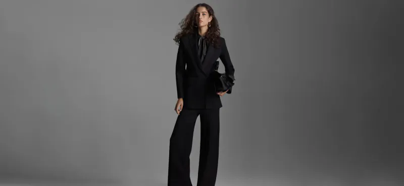Woman with curly hair poses confidently in black Scanlan Theodore suit and wide-leg pants