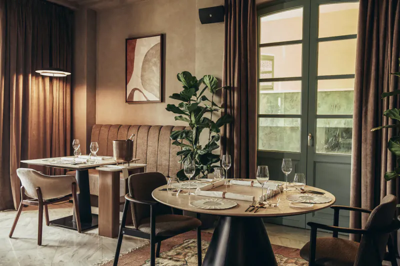 Elegant dining area at Makris Restaurant in Athens with round set table, wine glasses, plants, and large windows.
