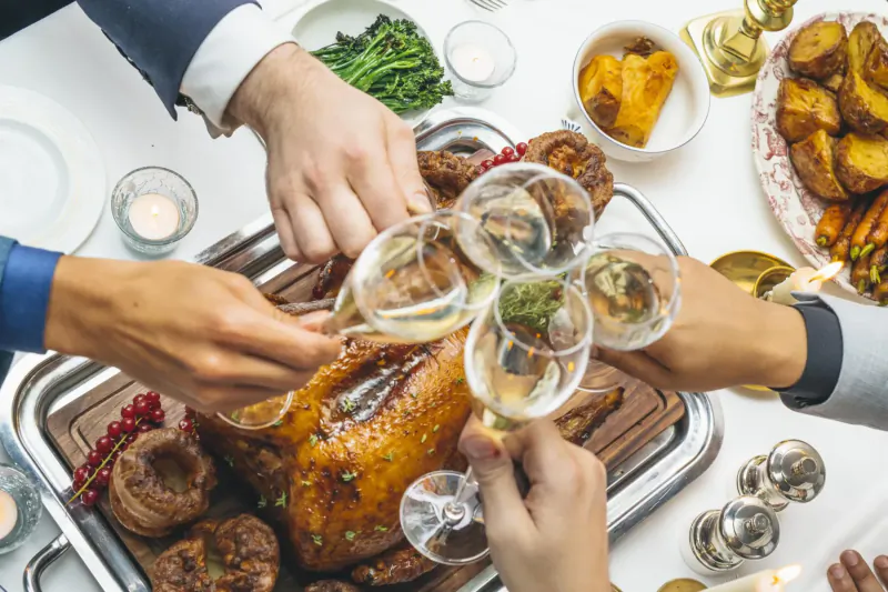 Group toasting with champagne glasses over roasted turkey and holiday feast on elegant table