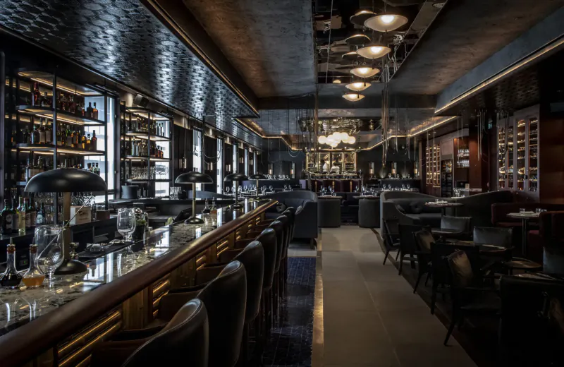 Elegant Lucky Cat Mayfair bar interior with black textured walls, pendant lights, wine racks, and leather stools.