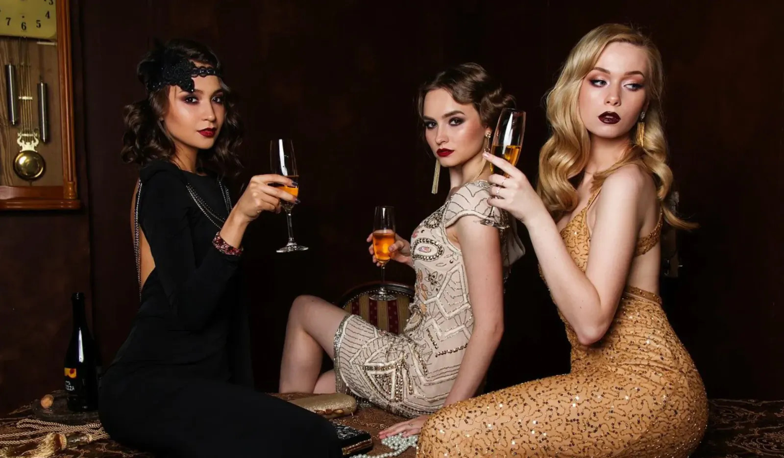 Three elegant women in glamorous 1920s dresses, holding champagne flutes, lounging luxuriously in a vintage room.