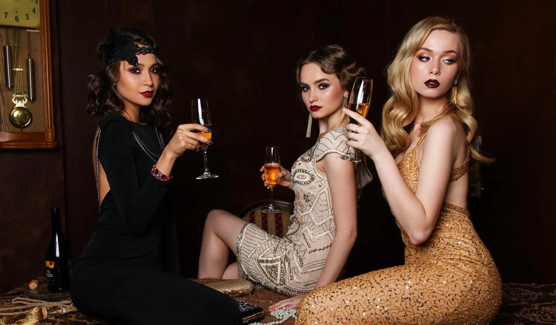 Three elegant women in glamorous 1920s dresses, holding champagne flutes, lounging luxuriously in a vintage room.