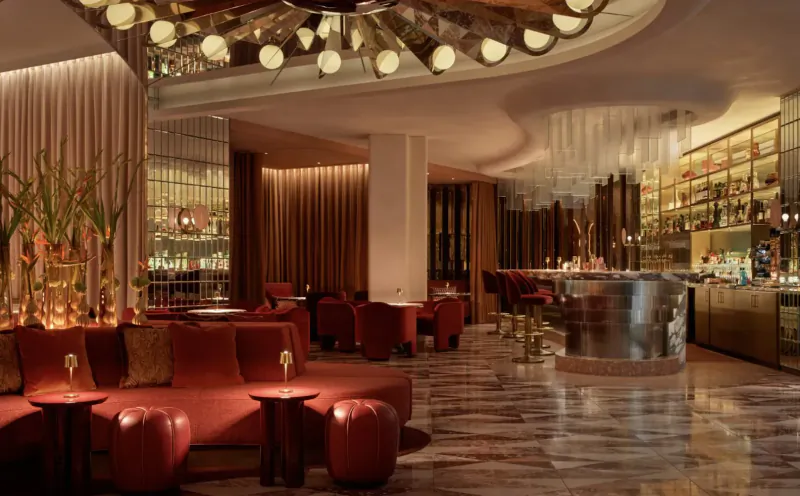 Elegant Revery Bar interior with curved red velvet seating, gleaming bar, pendant lights, and plants for afternoon tea.