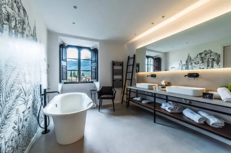 Elegant adults-only hotel bathroom in Majorca with freestanding tub, double sinks, towels, and mountain mural.