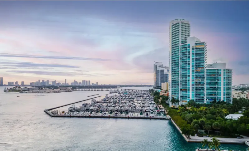 Murano's tall teal skyscrapers beside marina with yachts at sunset, Miami skyline and bay
