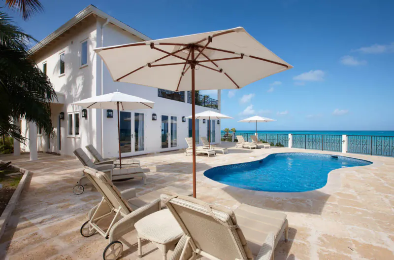 Blue Waters Resort & Spa Antigua: white luxury house with infinity pool, lounge chairs, umbrellas on terrace overlooking turquoise sea.