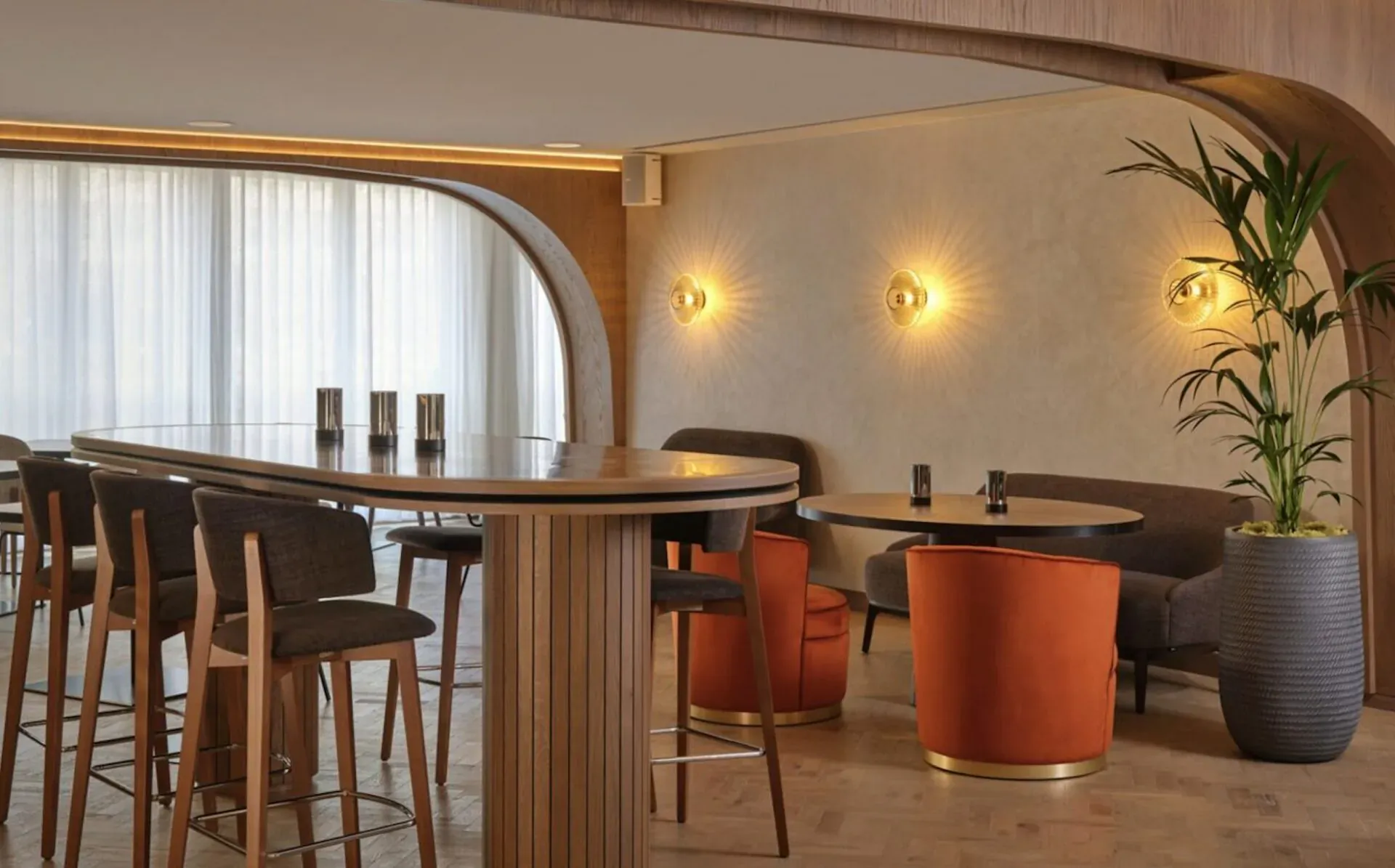 Modern canalside bar at The Reach at Piccadilly with curved wooden bar, orange chairs, plants, and warm lighting.