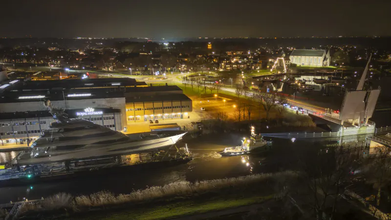 Aerial night view of urban canal with docked ships, lit buildings, and streets glowing yellow.