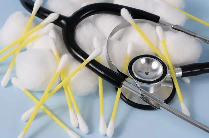 Black stethoscope surrounded by yellow-stick cotton swabs with white tips on blue background