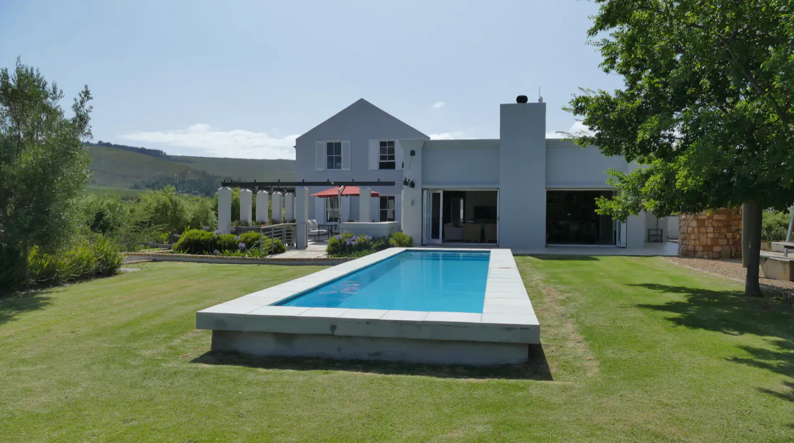 Modern white house with infinity pool, pergola, umbrella, and trees at South Hill Vineyards in Elgin Valley