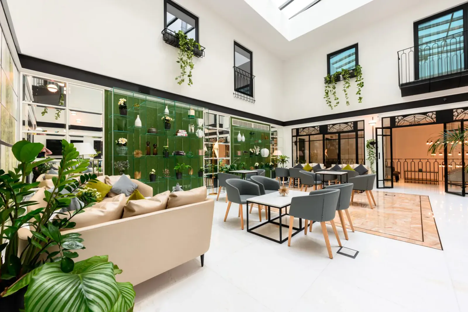 Modern Embassy Valletta Hotel atrium with green plant wall, beige sofa, dining chairs, tables, skylights, and courtyard doors.